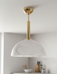 Lampa wisząca Klara z metalowym, złotym wykończeniem i białym kloszem w marmurowym wzorze. Zawieszona na długim, prostym uchwycie, w aranżacji nowoczesnej kuchni. Idealna do oświetlenia stołu.