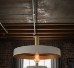 Lampa wisząca Dario z jedną oprawą E27 w kolorze białym z wewnętrzną złotą powłoką. Zawieszona na czarnym przewodzie, o okrągłym kształcie, z widoczną żarówką. Ujęcie z dołu, ukazujące detale konstrukcji oraz efektowne wykończenie.