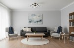 Lampa sufitowa Altea 3-punktowa w kolorze patyny, umieszczona na suficie, z trzema okrągłymi kloszami. W tle minimalistyczny salon z szarymi ścianami, szarym sofą, drewnianym stołem oraz regałem z książkami.