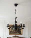 Cereus żyrandol świecznikowy 4xE14 w kolorze czarnym, z eleganckimi, zakrzywionymi ramionami i przezroczystymi żarówkami w kształcie łzy. Zawieszony na łańcuchu, w klasycznym stylu, idealny do aranżacji wnętrz. Tło z dekoracyjnymi detalami.
