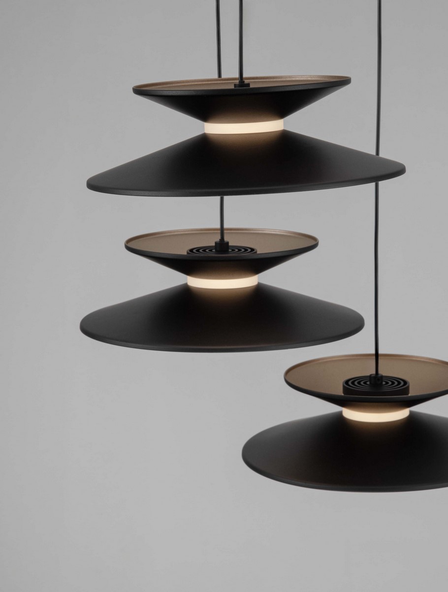 Lampa wisząca Guanay z pięcioma źródłami LED o mocy 24W. Kształt stożkowaty, w kolorze czarnym z złotymi detalami. Ułożona w trzech poziomach, z zintegrowanym oświetleniem. Zawieszona na cienkich linkach na jednolitym tle.