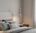 Lampa wisząca Arte z mosiądzu i fioletowego szkła, zawieszona nad łóżkiem w sypialni. Posiada dekoracyjne elementy w pastelowych kolorach, z widocznym kloszem w kształcie dzwonu i złotą podstawą. Tło to jasna ściana i stół nocny z filiżanką.