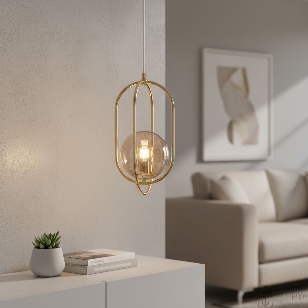 Lampa wisząca Binar 1-punktowa w kolorze złotym, z przezroczystą kulistą żarówką. Ujęcie z boku, zawieszona na białym przewodzie, w nowoczesnym wnętrzu z jasnym tłem i kanapą. Widoczna roślinka w doniczce oraz stos książek na białym meblu.