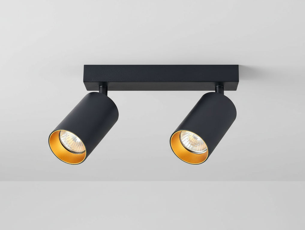 Czarna lampa sufitowa Eris z dwoma punktami świetlnymi, z metalowymi kloszami w formie cylindrów z wewnętrzną złotą powłoką. Zamontowana na prostokątnej podstawie, widok z dołu. Idealna do nowoczesnych wnętrz.