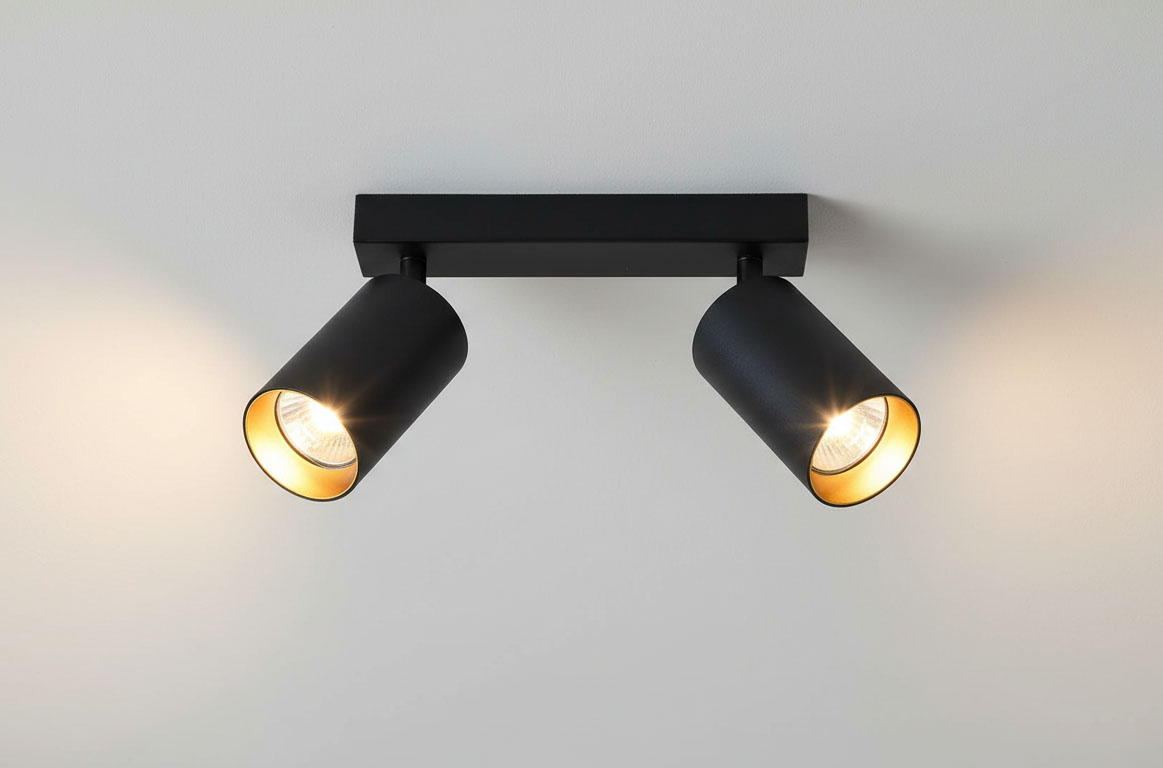 Czarna lampa sufitowa Eris z dwoma punktami świetlnymi, wykonana z metalu. Reflektory w formie cylindrów z wewnętrzną złotą powłoką, umieszczone na prostokątnej podstawie. Ujęcie frontalne, montowana na suficie.