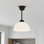 Lampa wisząca Frella z czarnym metalowym stelażem i białym, półkulistym kloszem z mlecznego szkła. Produkt zawieszony na długim pręcie, idealny do nowoczesnych wnętrz. Ujęcie z dołu, w jasnym otoczeniu kuchennym.