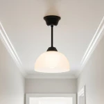 Czarna lampa wisząca Frella z kloszem w kształcie półkuli, wykonanym z matowego szkła. Zawieszona na cienkim, czarnym przewodzie. Ujęcie z dołu, na tle jasnego sufitu. Idealna do nowoczesnych wnętrz.