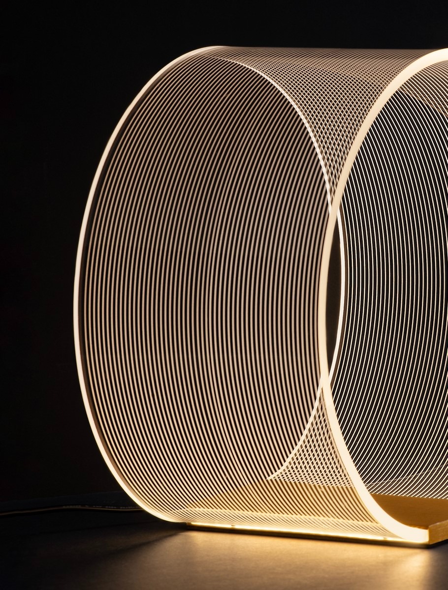 Lampa stołowa Huaral w kolorze złotym, z diodą LED 14W. Okrągła konstrukcja z cienkimi, metalowymi liniami, emitująca miękkie światło. Ujęcie z boku, na ciemnym tle, pokazujące detale wzoru i formy. Stabilna podstawa, nowoczesny design.
