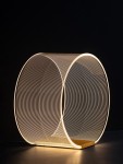 Lampa stołowa Huaral z jedną diodą LED 14W, w kształcie cylindrycznym, wykonana z cienkiej, złotej siatki. Źródło światła emituje ciepłe światło, a elegancka podstawa podkreśla nowoczesny design. Ujęcie z boku na ciemnym tle.