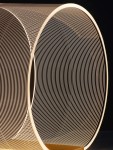 Lampa stołowa Huaral z 1xLED 14W w złotej obudowie. Wygięta struktura z cienkich linii, emitująca ciepłe światło. Widok z boku, podkreślający nowoczesny design i teksturę materiału. Tło ciemne, co uwydatnia kształt lampy.