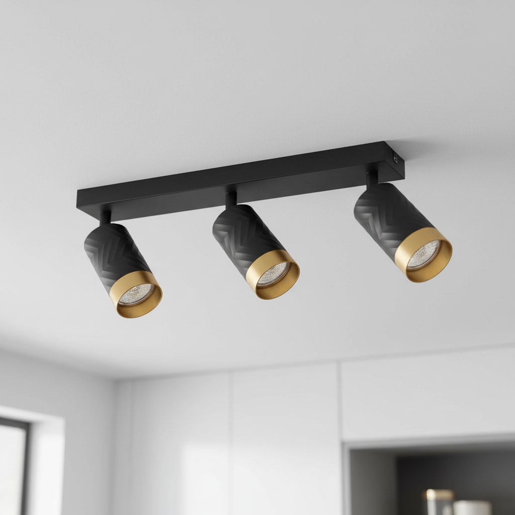 Lampa sufitowa Arras z trzema reflektorami GU10 w kolorze czarnym i złotym. Reflektory o fakturze w geometryczny wzór, zamontowane na prostokątnej, czarnej podstawie. Ujęcie z dołu, pokazujące położenie lampy na suficie.