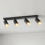 Czarna lampa sufitowa Arras z czterema spotami GU10. Lampy mają teksturowane, cylindryczne klosze w kolorze czarnym z złotym wykończeniem. Ułożona poziomo na suficie, oświetla wnętrze, dodając nowoczesnego stylu.