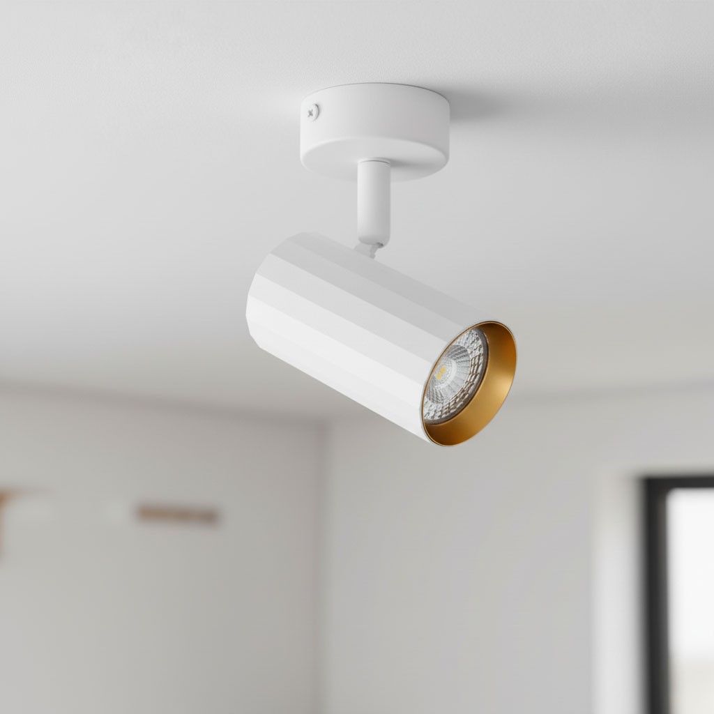 Lampa sufitowa Nicea w kolorze białym i złotym z jedną oprawą GU10. Kształt cylindryczny z teksturą w poziome paski, zamontowana pod kątem na białym uchwycie. Na tle jasnego wnętrza, z widoczną żarówką w środku.