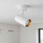 Lampa sufitowa Nicea w kolorze białym i złotym z jedną oprawą GU10. Kształt cylindryczny z teksturą w poziome paski, zamontowana pod kątem na białym uchwycie. Na tle jasnego wnętrza, z widoczną żarówką w środku.