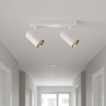 Lampa sufitowa Nicea w kolorze białym z złotymi akcentami, wyposażona w dwa reflektory GU10. Ujęcie z dołu, pokazujące lampę zamontowaną na suficie w korytarzu. Wysokie, cylindryczne klosze z błyszczącym wykończeniem.
