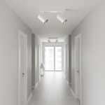 Lampa sufitowa Nicea z dwoma spotami GU10 w białej obudowie z złotym wnętrzem, zamontowana na suficie w jasnym korytarzu, oświetlająca przestrzeń. W tle widoczne drzwi i okna, na podłodze jasne deski.