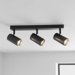 Lampa sufitowa Nicea w kolorze czarnym i złotym, z trzema reflektorami GU10. Ułożona poziomo na suficie, z cylindrycznymi kloszami w czerni i złotych detalach, emitującymi światło. Tło jasne, minimalistyczne.