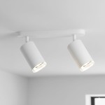 Biała lampa sufitowa Turyn IP44 z dwoma regulowanymi spotami na żarówki GU10. Ujęcie z dołu, pokazujące cylindryczne klosze, zamontowane na prostokątnej podstawie, w jasnym wnętrzu.