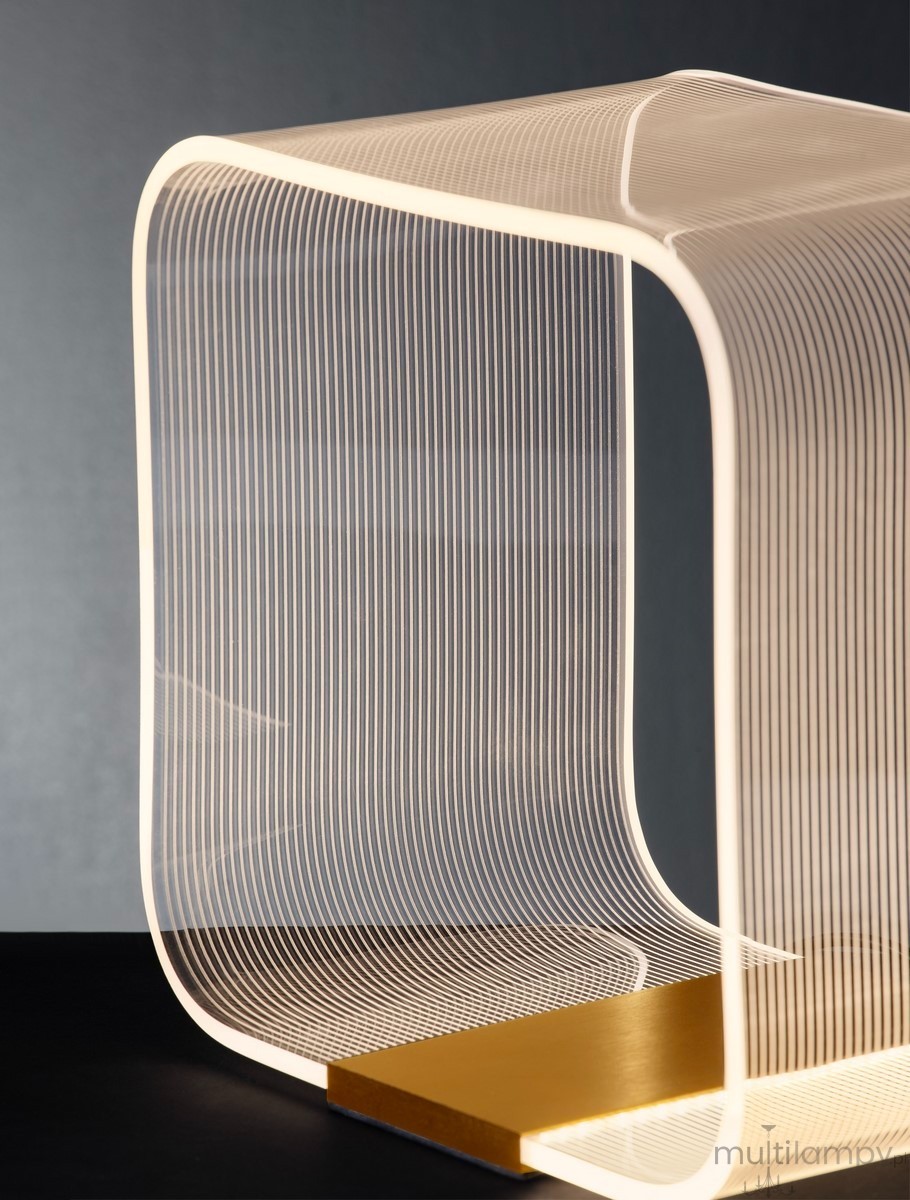 Lampa stołowa Huaral 1xLED 14W w złotej podstawie, z przezroczystym, falującym kloszem z linii. Ujęcie frontalne, ukazujące elegancką formę i strukturę materiału. Tło w odcieniach szarości podkreśla nowoczesny design.