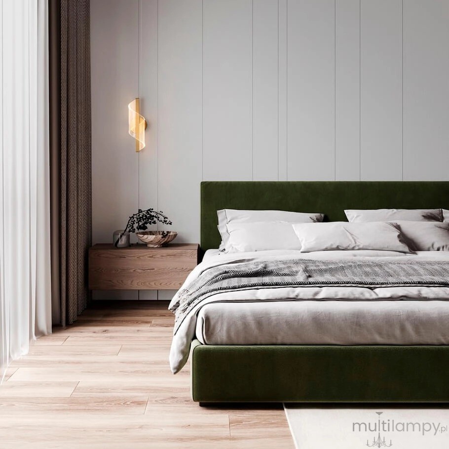 Huaral kinkiet 1xLED 9W w kolorze złotym, zamontowany na ścianie obok łóżka. Lampa ma nowoczesny, spiralny kształt, emitująca ciepłe światło. W tle widoczna jest zielona tapicerowana rama łóżka oraz drewniana szafka nocna.