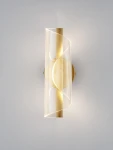 Huaral kinkiet 1xLED 9W w kolorze złotym. Lampa ma nowoczesny, falisty klosz z transparentnego materiału oraz metalową podstawę. Ujęcie frontalne, kinkiet zamontowany na ścianie, emituje ciepłe światło. Tło w jasnym kolorze.