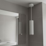 Lampa wisząca Turyn IP44 w kolorze białym, o cylindrycznym kształcie, zawieszona na cienkim przewodzie. Widoczna w nowoczesnej łazience z szarymi płytkami, podświetlenie od dołu. W tle lustro i umywalka.