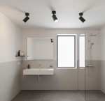 Czarna lampa sufitowa Turyn IP44 z pojedynczym reflektorem GU10, zamontowana na suficie w nowoczesnej łazience. Widoczne są trzy lampy, oświetlające przestrzeń nad umywalką i prysznicem, w minimalistycznym, jasnym wnętrzu.