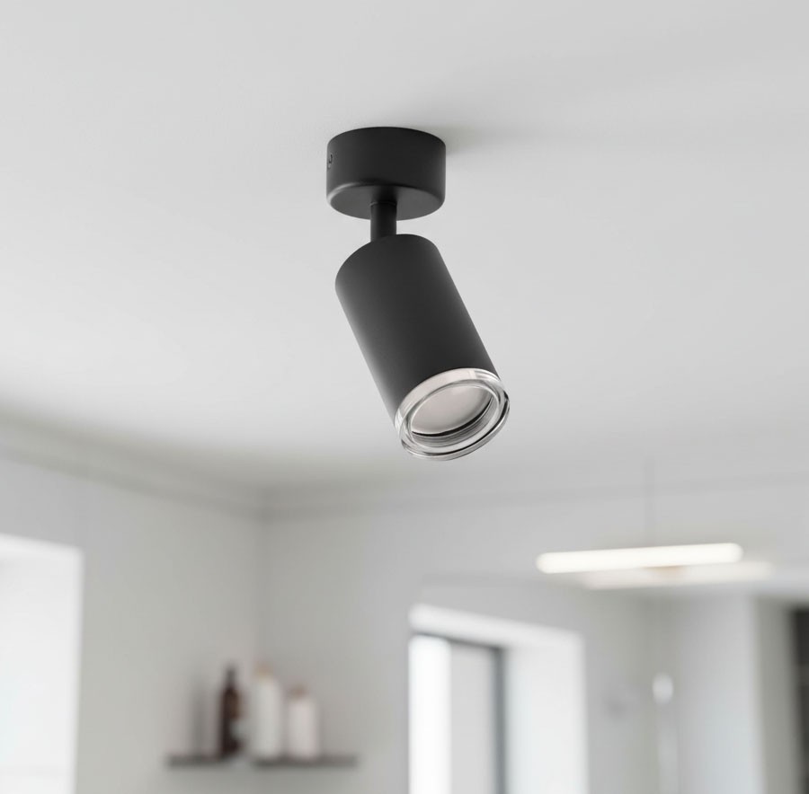 Czarna lampa sufitowa Turyn IP44 w formie spotu z jednym gniazdem GU10. Ujęcie z dołu, lampa zamontowana na suficie, o cylindrycznym kształcie z przezroczystym kloszem, emitującym światło. Tło jasne, minimalistyczne.