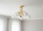 Lampa wisząca Eryka w kolorze złotym z pięcioma kloszami w kształcie półkul, wykonanymi z białego szkła. Produkt zamontowany na suficie, z widocznym metalowym stelażem i eleganckim, nowoczesnym designem.