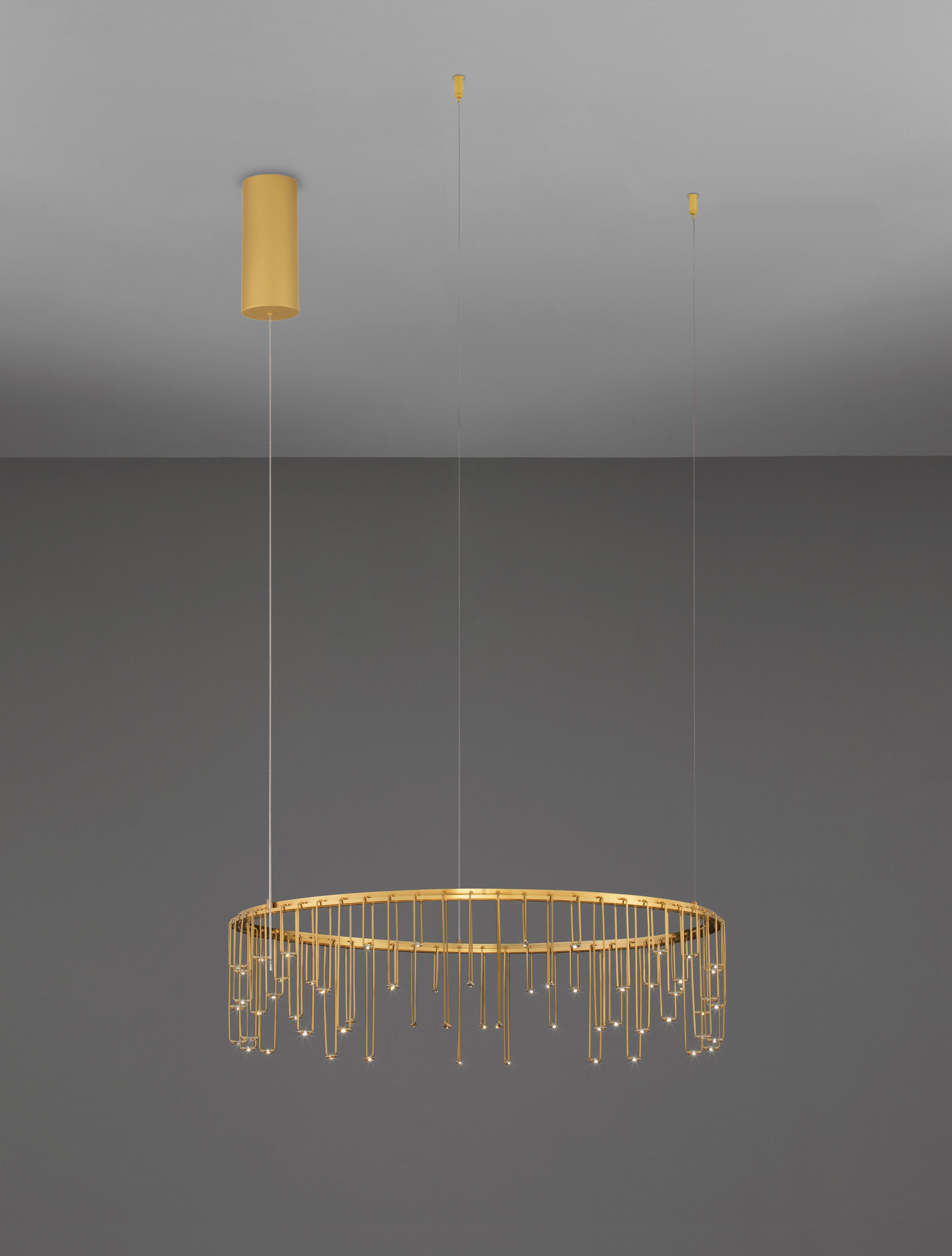 Lampa wisząca Huaraz D65 z 1xLED 26W, w kolorze złotym. Okrągła konstrukcja z długimi, prostokątnymi elementami, zawieszona na cienkich linkach. Górna część w formie cylindrycznej osłony. Tło w odcieniach szarości, podkreślające elegancki design.