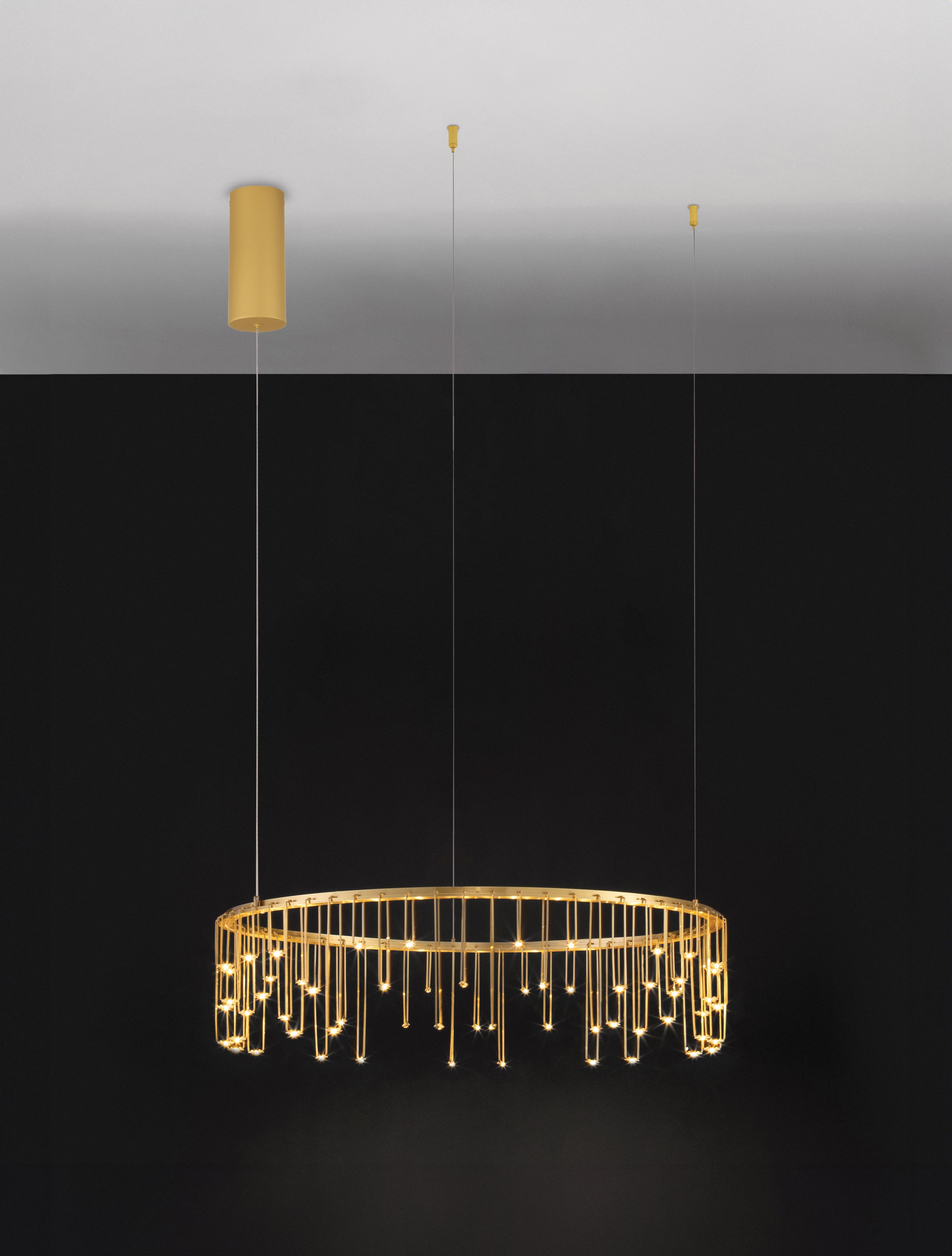 Lampa wisząca Huaraz D65, 1xLED 26W, w złotej kolorystyce. Okrągła forma z wiszącymi elementami świetlnymi, zamontowana na dwóch cienkich linkach. Tło czarne, sufit z okrągłym mocowaniem w tym samym kolorze.
