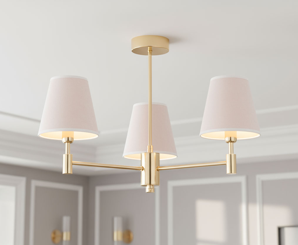 Żyrandol Astrit w kolorze złotym, z trzema abażurami w delikatnym różowym odcieniu. Ułożony w formie rozłożonej, z abażurami skierowanymi w dół. Prosta konstrukcja z metalowym stelażem, idealny do nowoczesnych wnętrz.