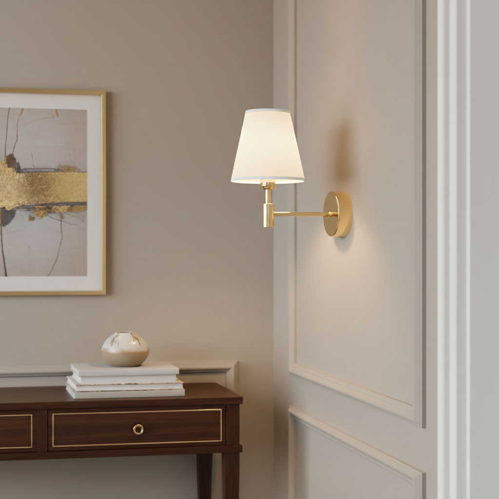 Kinkiet Astrit 1xE14 w kolorze złotym, z białym abażurem w kształcie stożka, zamontowany na ścianie. Obok widoczna drewniana komoda z dekoracyjnymi przedmiotami. Tło w neutralnym odcieniu, co podkreśla elegancję lampy.
