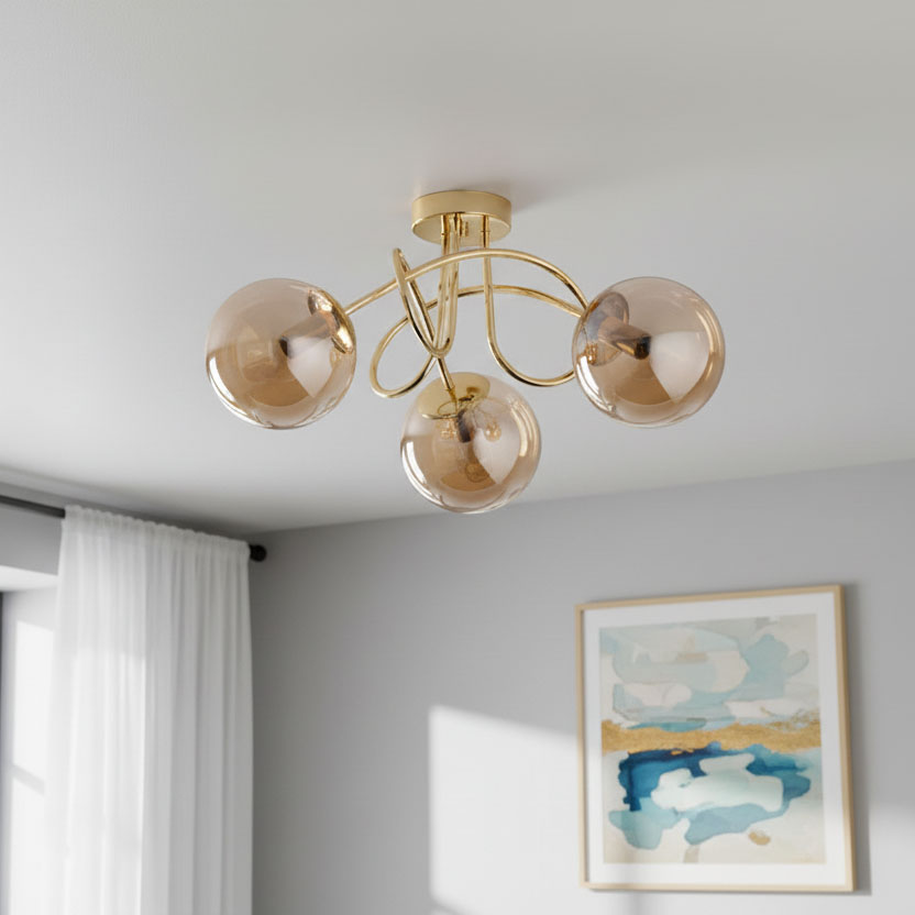 Lampa sufitowa Banko 3xE14 w kolorze złotym, z trzema okrągłymi kloszami w odcieniu przezroczystego brązu, zamontowana na suficie. Widok z dołu, z widocznymi dekoracyjnymi, zakrzywionymi ramionami. Tło w jasnoszarym kolorze z obrazem na ścianie.