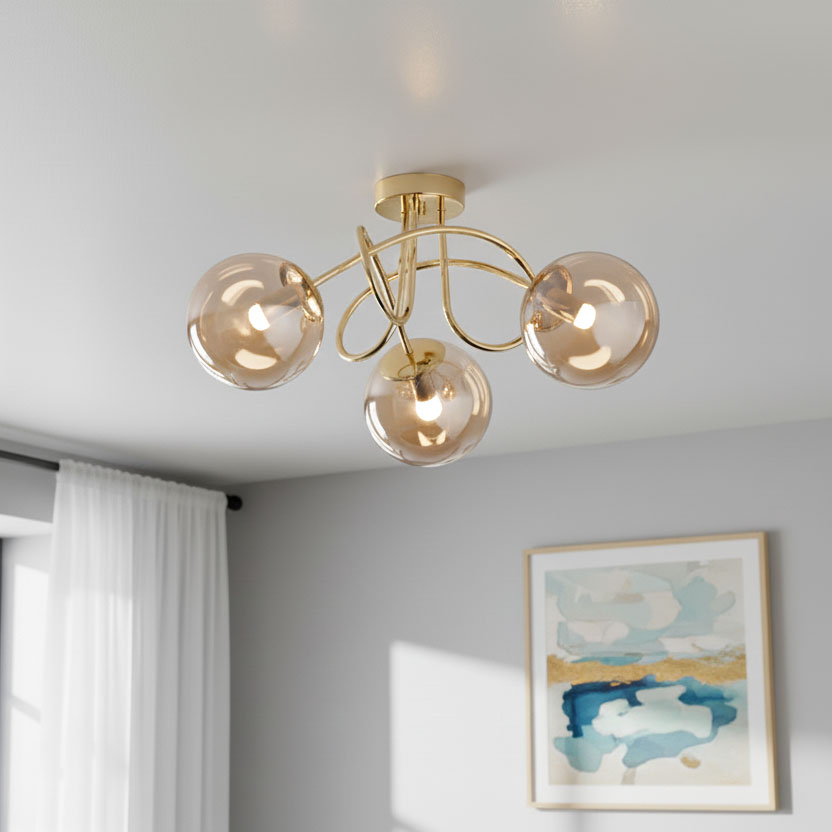 Lampa sufitowa Banko z trzema źródłami światła E14, w złotym kolorze. Kształt z delikatnymi, zaokrąglonymi kloszami w odcieniu przezroczystym. Montowana na suficie, z dekoracyjnymi, falistymi ramionami. Tło w jasnych tonacjach z obrazem na ścianie.