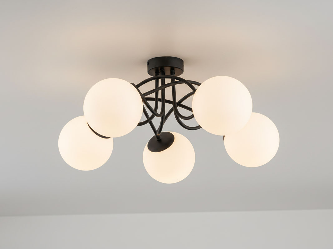 Czarna lampa sufitowa Banko z pięcioma okrągłymi kloszami w kolorze białym, zamontowana na suficie. Klosze umieszczone na metalowych ramionach tworzą nowoczesny design. Wymiary i szczegóły konstrukcji nie są widoczne.