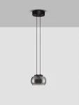 Lampa wisząca Huarmey z czarnym metalowym mocowaniem i przezroczystym kloszem w kształcie elipsy, zawieszona na dwóch cienkich linkach. Używa 1 żarówki LED 9W. Tło w jasnym kolorze.