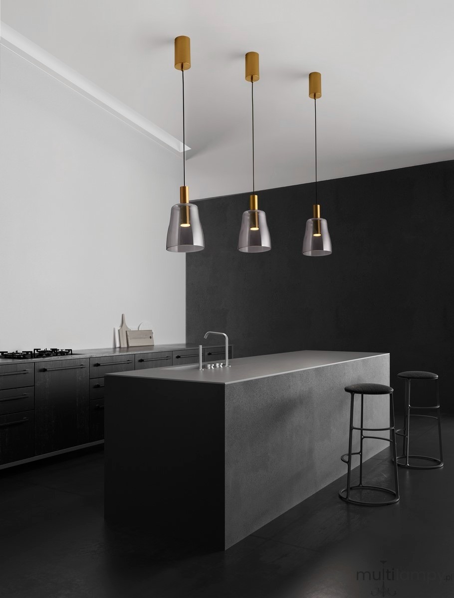 Lampa wisząca Iquitos 1xLED 7W w kolorze złotym, z przezroczystym kloszem, zawieszona na cienkich linkach. Widoczna w nowoczesnej kuchni nad wyspą, w otoczeniu czarnych stołków barowych i minimalistycznej zabudowy.