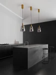 Lampa wisząca Iquitos 1xLED 7W w kolorze złotym, z przezroczystym kloszem, zawieszona na cienkich linkach. Widoczna w nowoczesnej kuchni nad wyspą, w otoczeniu czarnych stołków barowych i minimalistycznej zabudowy.