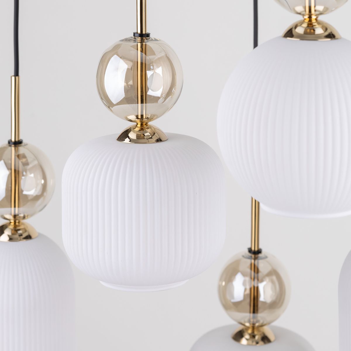 Lampa wisząca Sophia z sześcioma źródłami E14, w białym kolorze. Składa się z cylindrycznych kloszy z teksturowanej białej ceramiki oraz przezroczystych kulistych elementów, wykończona złotymi detalami. Ujęcie w zbliżeniu, na jednolitym tle.