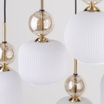 Lampa wisząca Sophia z sześcioma źródłami E14, w białym kolorze. Składa się z cylindrycznych kloszy z teksturowanej białej ceramiki oraz przezroczystych kulistych elementów, wykończona złotymi detalami. Ujęcie w zbliżeniu, na jednolitym tle.