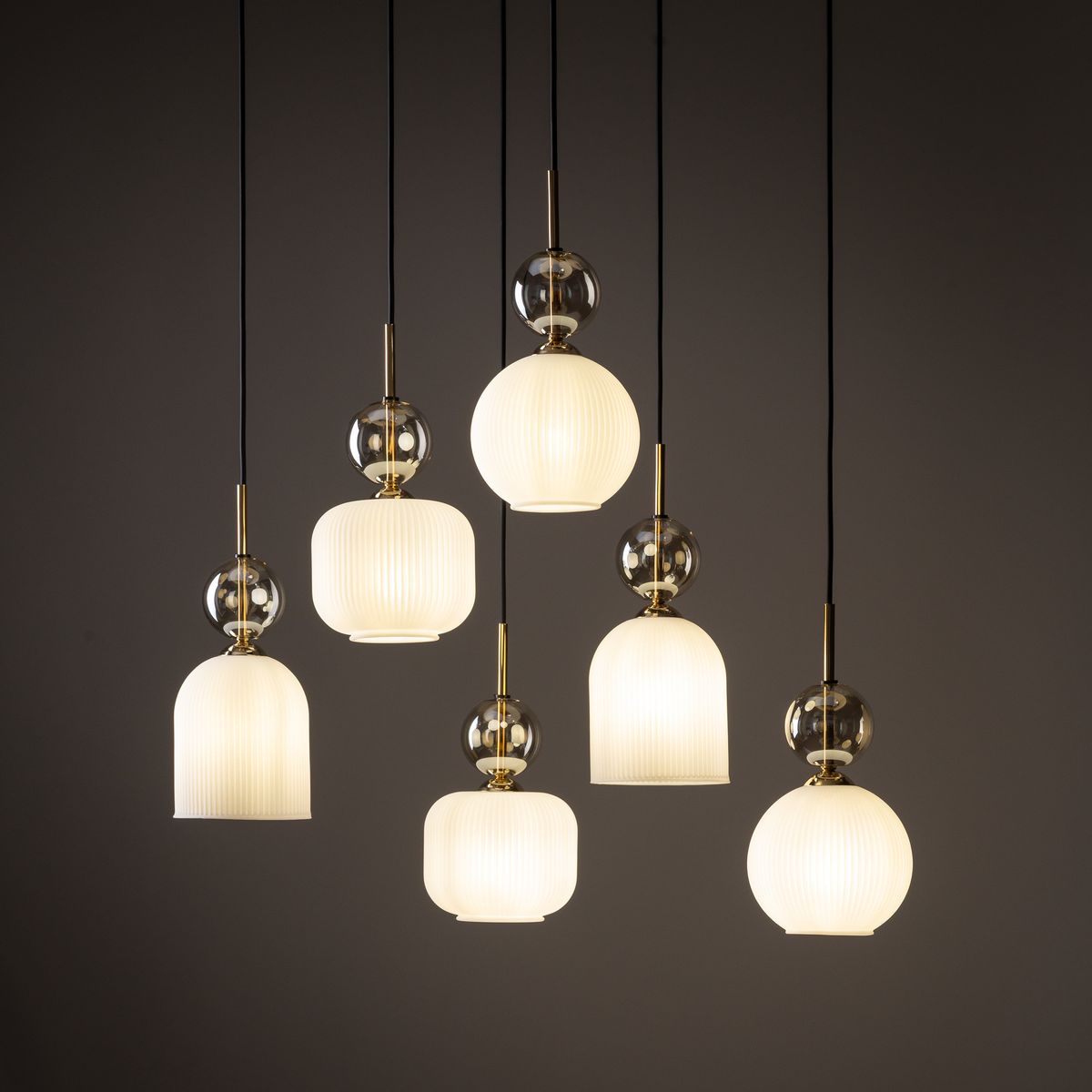Lampa wisząca Sophia z sześcioma źródłami światła E14, w białej oprawie. Posiada różne kształty kloszy: cylindryczny, kulisty oraz prostokątny, z dekoracyjnymi elementami w kolorze złotym i przezroczystymi akcentami. Zawieszona na czarnych przewodach.