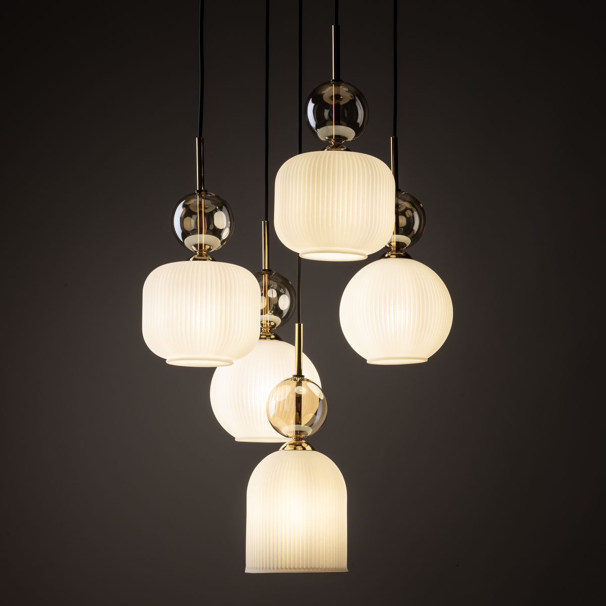 Lampa wisząca Sophia z pięcioma kloszami w kolorze białym, wykonana z materiału o fakturze prążkowanej. Klosze różnej wielkości zawieszone na czarnych przewodach, z metalowymi elementami w złotym kolorze. Przeznaczona na żarówki E14.