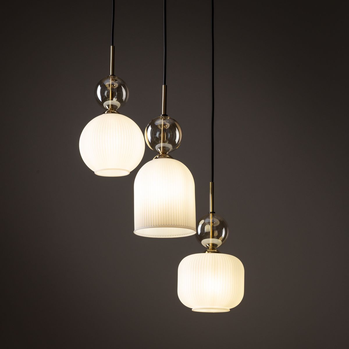 Biała lampa wisząca Sophia z trzema kloszami E14, w tym okrągłym i dwiema cylindrycznymi, z przezroczystymi detalami. Zawieszona na czarnych kablach, o matowej fakturze, idealna do nowoczesnych wnętrz.