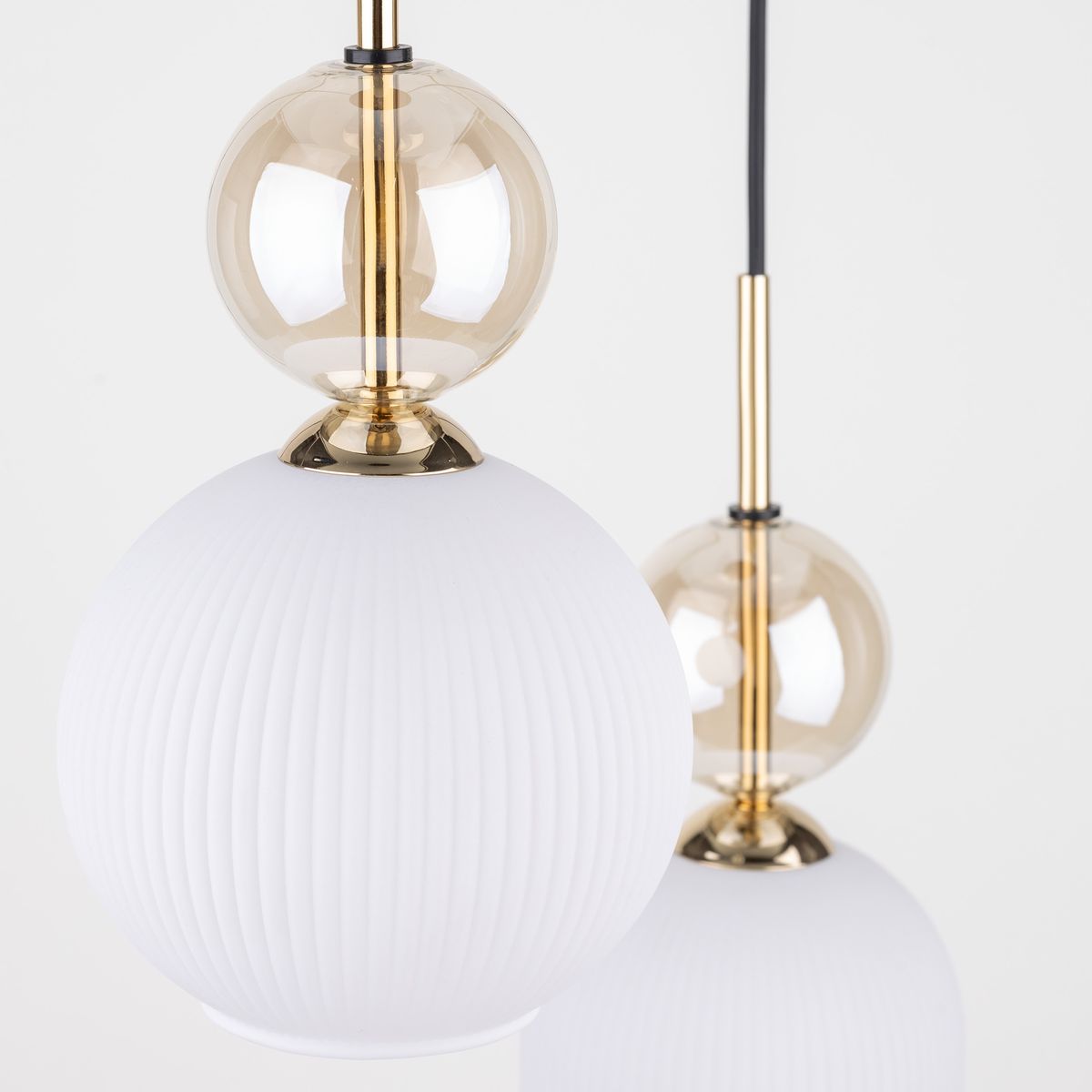 Biała lampa wisząca Sophia z trzema źródłami światła E14, z okrągłymi, matowymi kloszami w formie kul oraz przezroczystymi, szklanymi elementami w kolorze złotym. Ujęcie z przodu, z widocznymi detalami faktury kloszy.