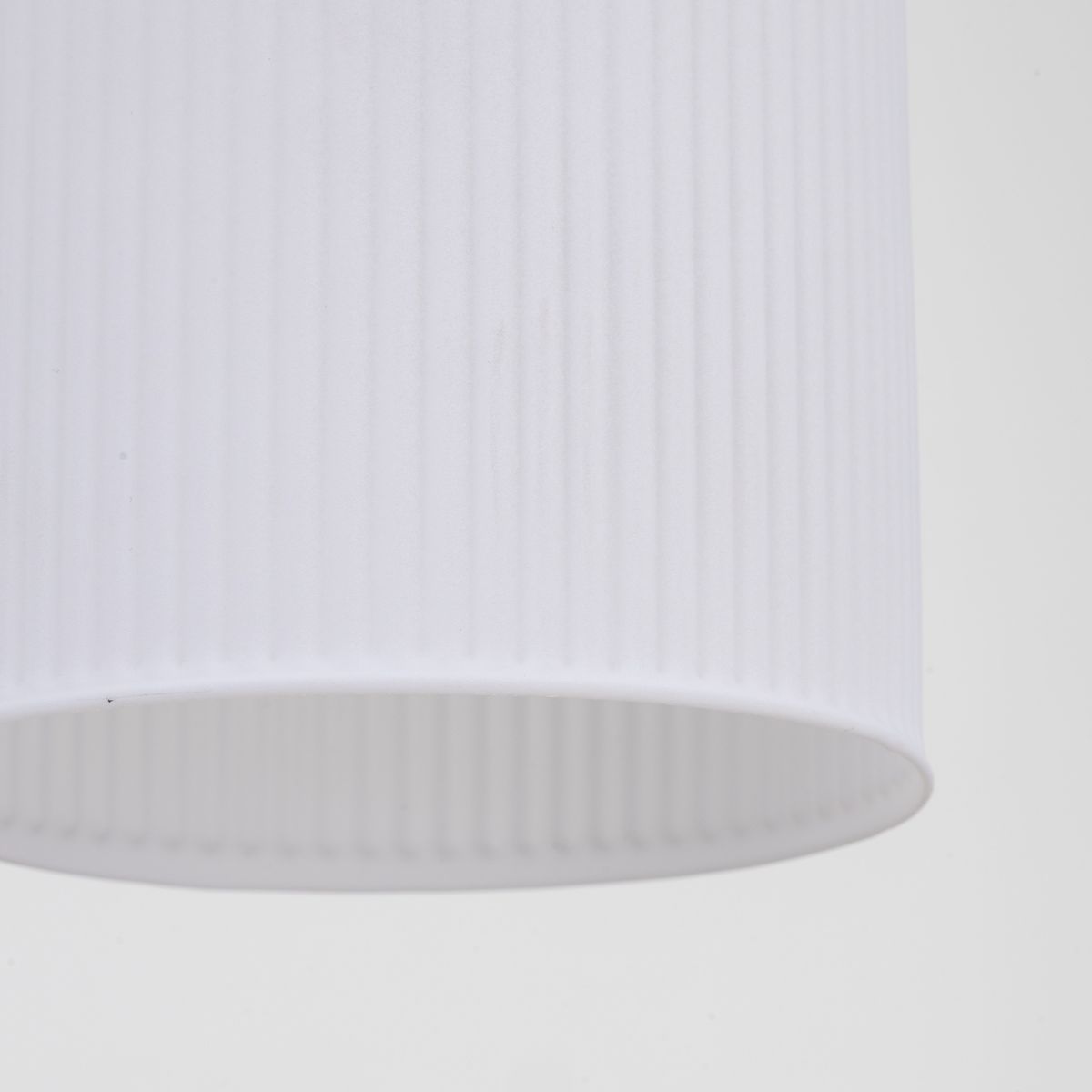 Biała lampa wisząca Sophia z abażurem w pionowe żłobienia. Ujęcie z bliska, pokazujące górną część klosza. Przeznaczona na trzy żarówki E14. Prostokątny kształt, minimalistyczny design, idealna do nowoczesnych wnętrz.