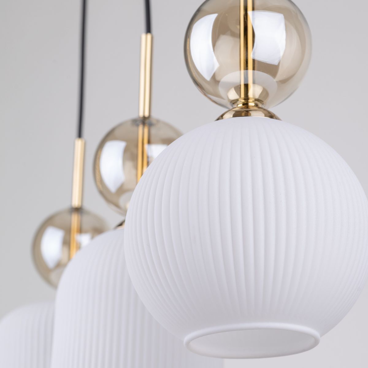 Lampa wisząca Sophia 3xE14 w kolorze białym. Składa się z trzech okrągłych kloszy z matowego szkła z pionowymi żłobieniami oraz przezroczystych kul, zawieszonych na czarnym przewodzie. Elementy metalowe w kolorze złotym.
