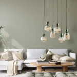 Lampa wisząca Sophia z sześcioma kloszami w kolorze bursztynowym i zielonym, zawieszona na czarnych przewodach. Klosze mają fakturę w pionowe prążki. Produkt umieszczony nad sofą w jasnym wnętrzu z roślinami i drewnianym stolikiem.