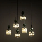 Lampa wisząca Sophia z sześcioma kloszami E14, w kolorze bursztynowym i zielonym. Klosze mają prążkowaną fakturę oraz kuliste, błyszczące elementy. Produkt zwisający na cienkich linkach, umieszczony na ciemnym tle.