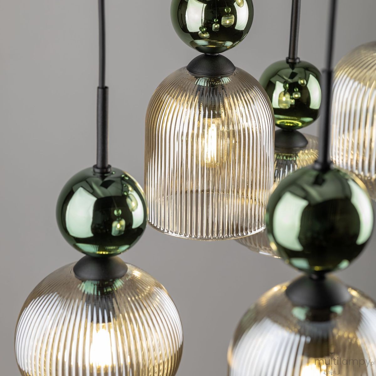 Lampa wisząca Sophia 6xE14, składająca się z bursztynowych kloszy z pionowymi żłobieniami oraz zielonych, szklanych kul. Elementy zawieszone na czarnym przewodzie, w nowoczesnym stylu, idealne do eleganckich wnętrz. Tło szare.